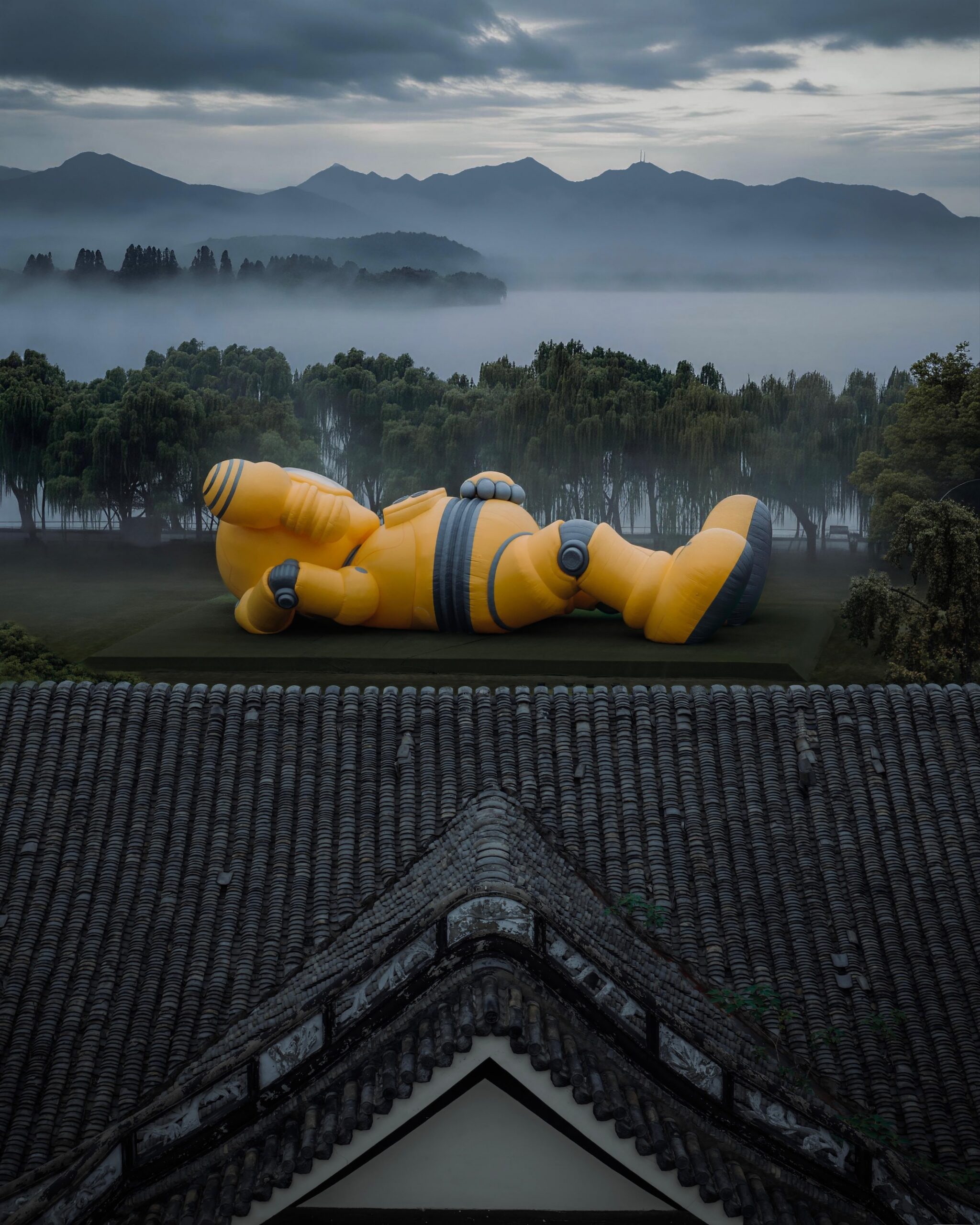 The sculpture seen over a traditional Chinese tiled roof, willow trees and the misty lake beyond