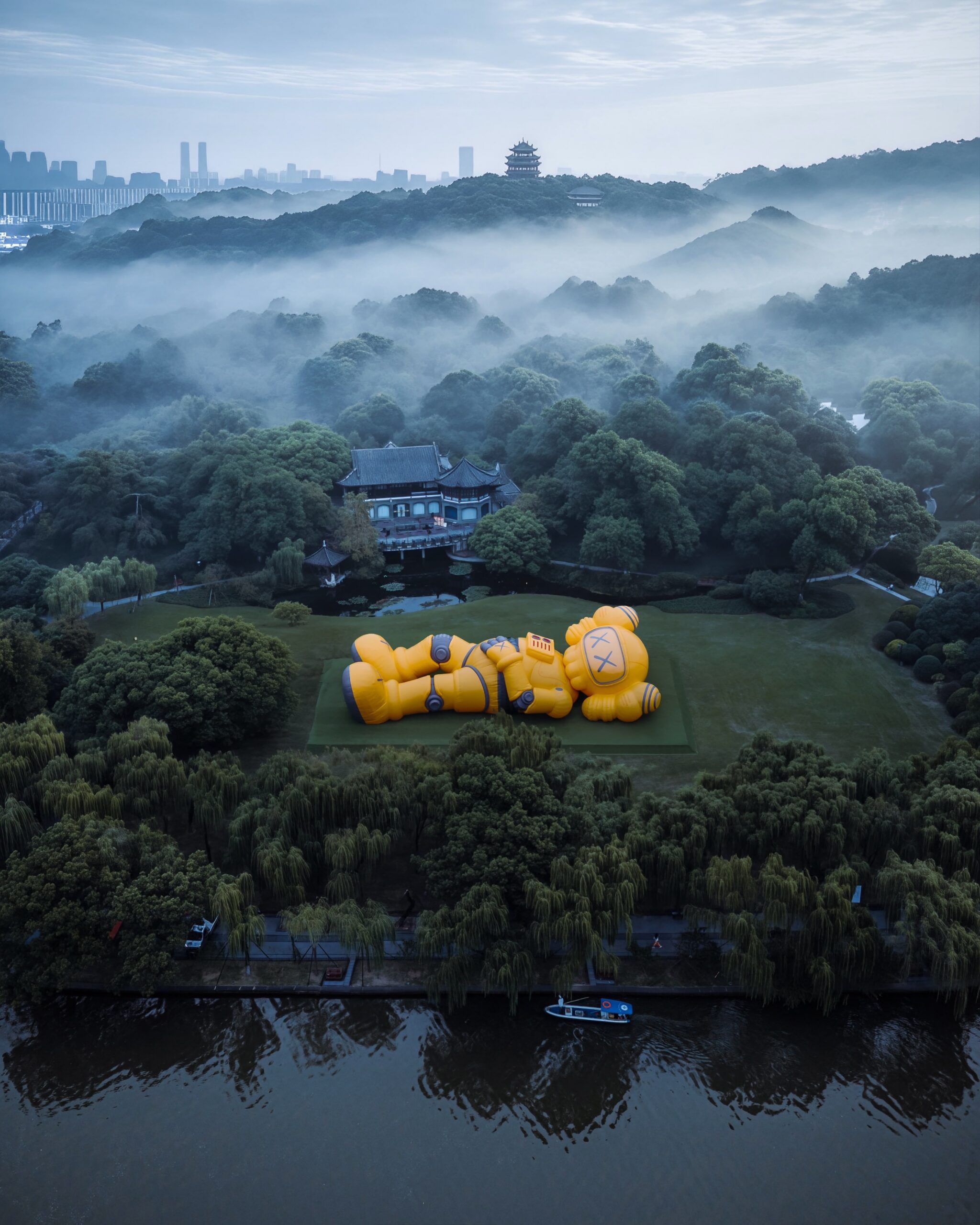 Wide aerial view of the installation with West Lake in the foreground and the Hangzhou skyline dissolving into mist