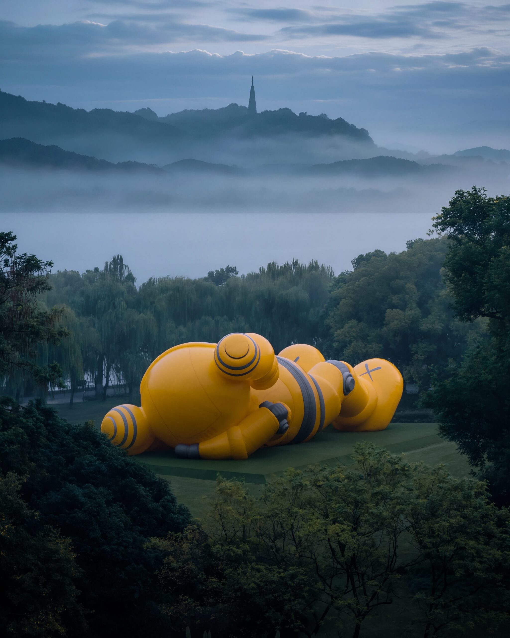 The sculpture from behind, facing the mist-shrouded lake and a distant pagoda