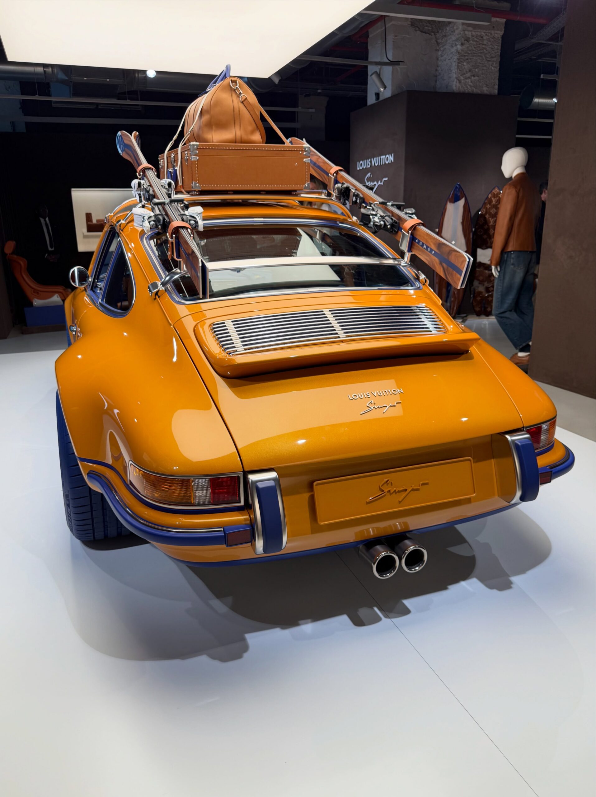 Rear three-quarter of the orange 911 with LV trunk and skis on roof rack